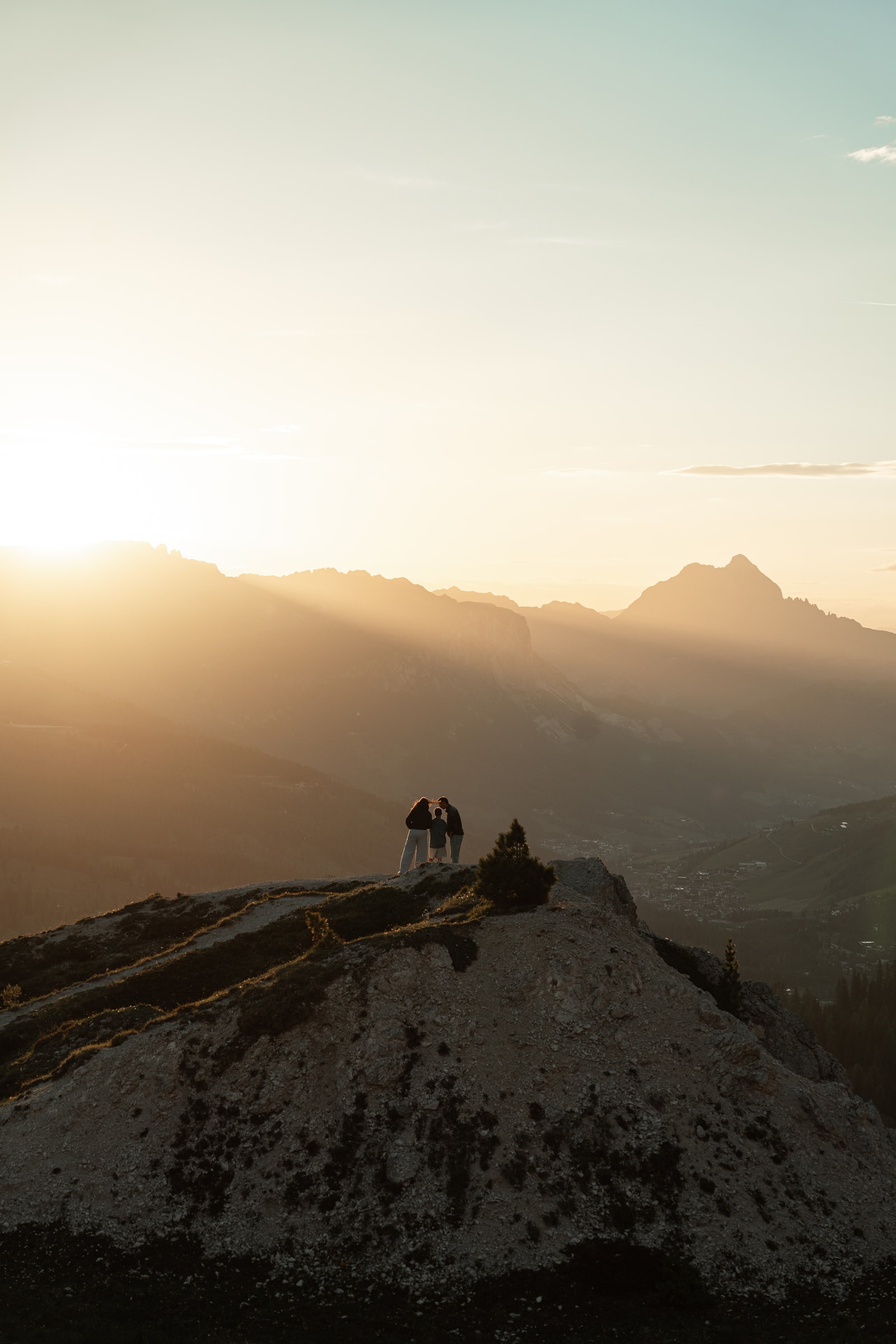 Figure in controluce su un crinale montuoso, con raggi di sole sulla valle.