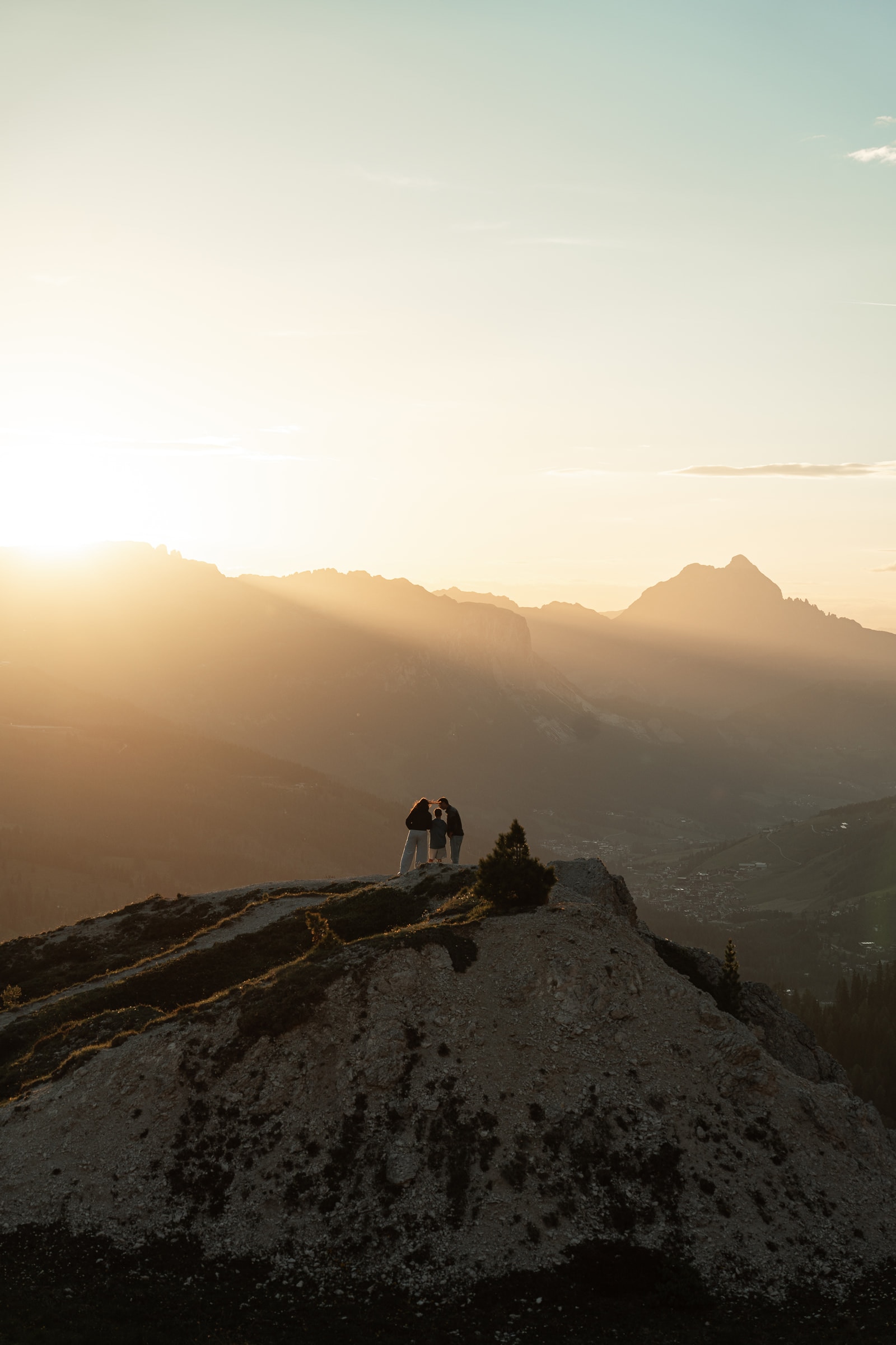 Figure in controluce su un crinale montuoso, con raggi di sole sulla valle.